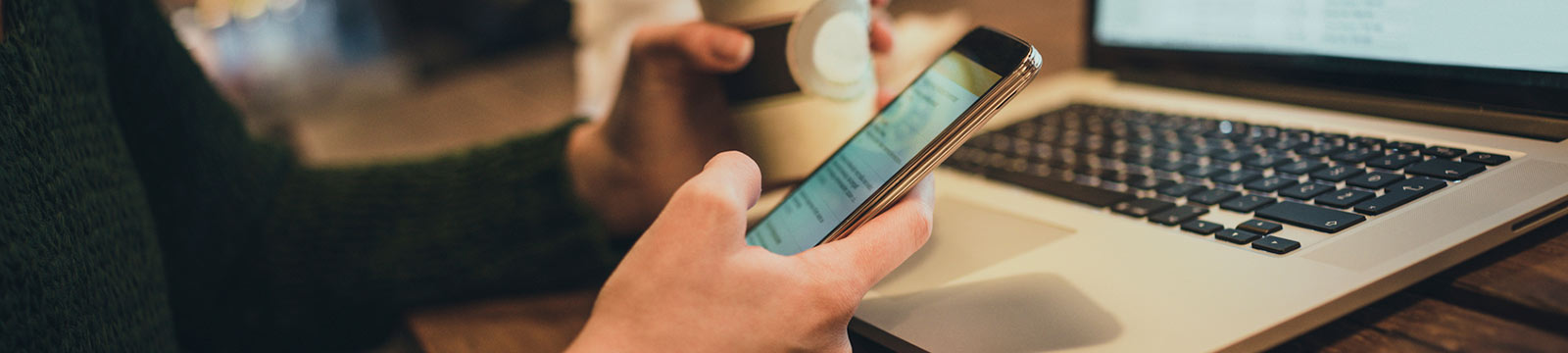 a person holding a cup of coffee and their mobile phone