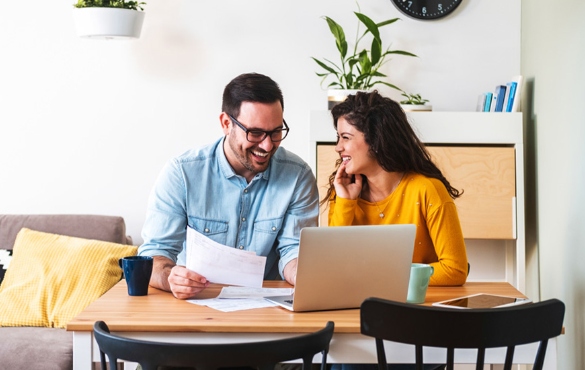 A smiling couple reviewing documents in front of their laptop.